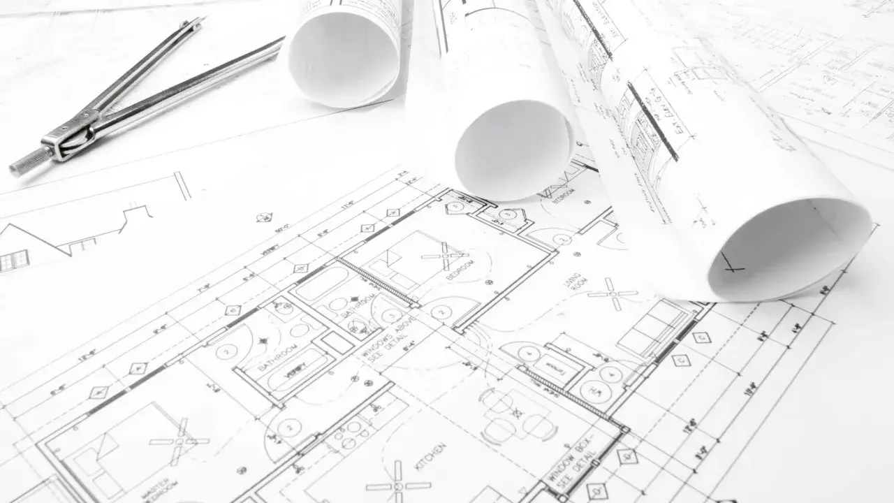 Projekt budowlany domu z widocznym cyrklem i zwiniętymi planami.