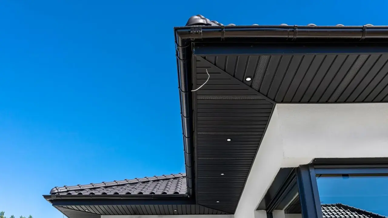 Nowoczesna podbitka tynkowana w kolorze czarnym, zintegrowana z czarną rynną i dachówką. Wbudowane oświetlenie podkreśla architekturę.