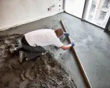 Budowlaniec wyrównuje świeży jastrych drewnianą łatą.