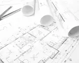 Projekt budowlany domu z widocznym cyrklem i zwiniętymi planami.