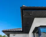 Nowoczesna podbitka tynkowana w kolorze czarnym, zintegrowana z czarną rynną i dachówką. Wbudowane oświetlenie podkreśla architekturę.