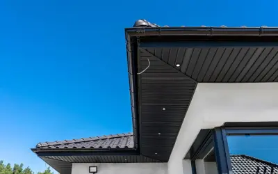 Nowoczesna podbitka tynkowana w kolorze czarnym, zintegrowana z czarną rynną i dachówką. Wbudowane oświetlenie podkreśla architekturę.