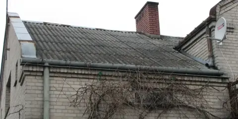 Stary dach z azbestu, pokryty falistymi płytami, z kominem i anteną satelitarną. Pnącza oplatają ścianę.