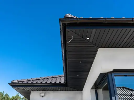 Nowoczesna podbitka tynkowana w kolorze czarnym, zintegrowana z czarną rynną i dachówką. Wbudowane oświetlenie podkreśla architekturę.