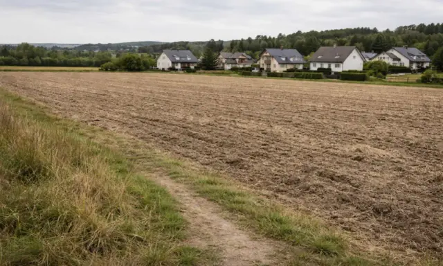 Pola po odrolnieniu działki, gotowe pod budowę domów. W tle widać zabudowania i las.