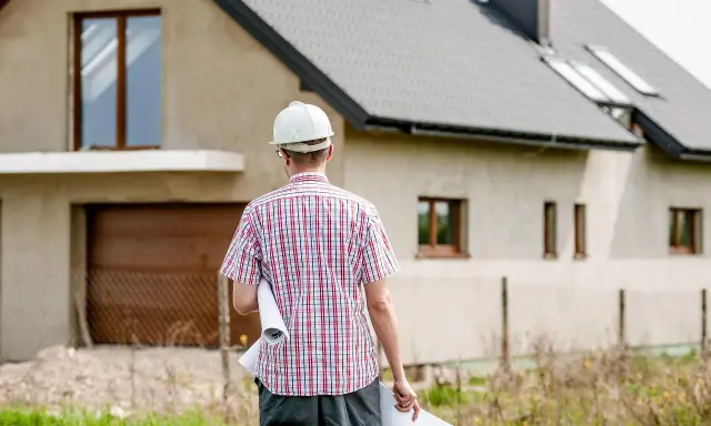 Inżynier w kasku z planami w ręku analizuje kosztorys inwestorski budowy domu.