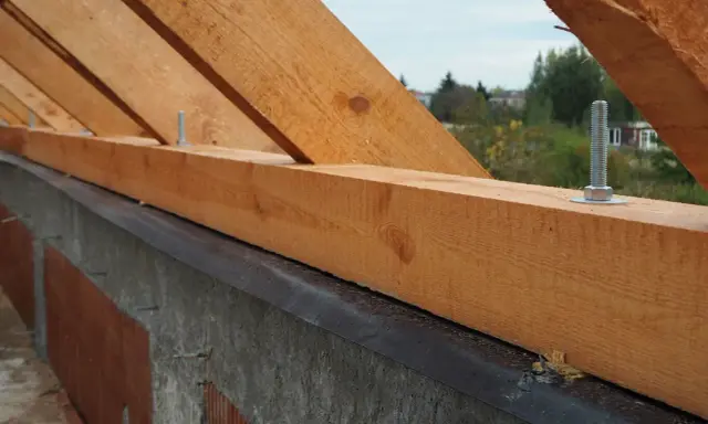 Murłata, drewniana belka na ścianie, stanowi podstawę więźby dachowej. Widać śruby mocujące ją do konstrukcji.