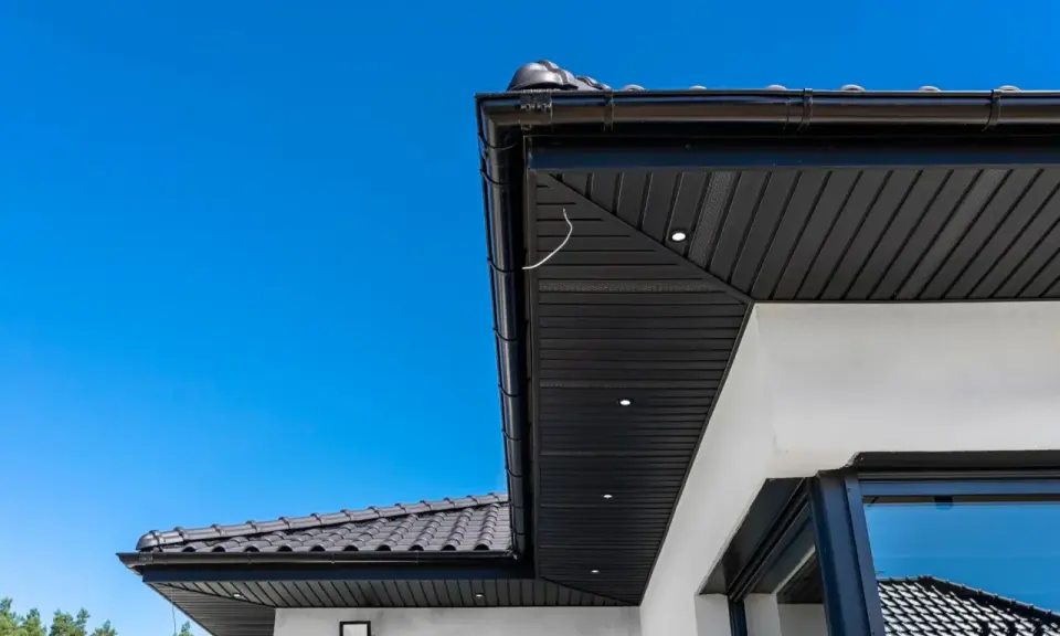 Nowoczesna podbitka tynkowana w kolorze czarnym, zintegrowana z czarną rynną i dachówką. Wbudowane oświetlenie podkreśla architekturę.
