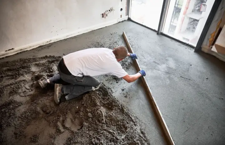 Budowlaniec wyrównuje świeży jastrych drewnianą łatą.
